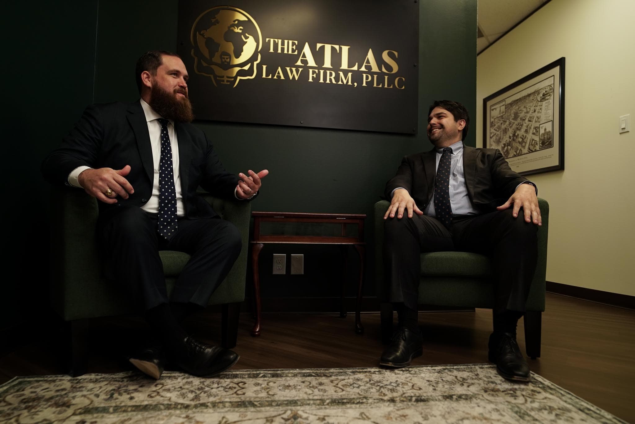 Two Atlas Law Firm attorneys in conversation beneath the firm's brand wall.